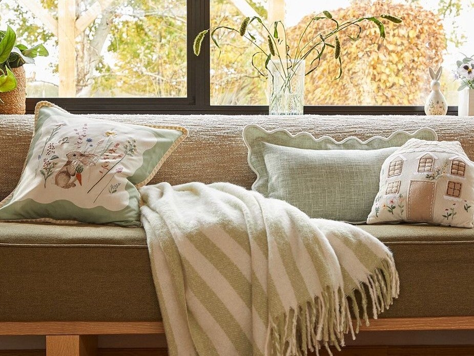 Bunny cuddle cushion and bunny cushion on top of a bed with Easter themed bedding.