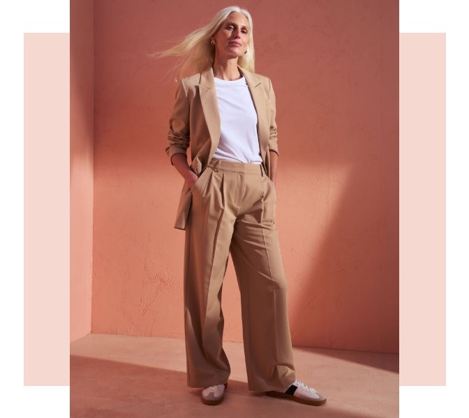 Woman wearing beige wide leg trousers with a matching blazer and white t shirt and trainers