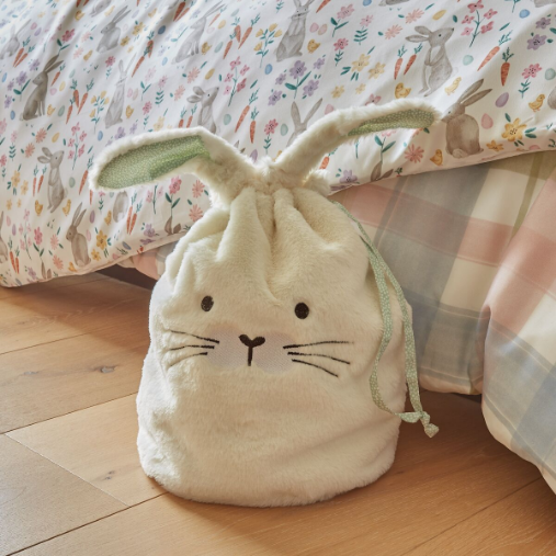 A white bunny rabbit themed sack next to a bed.