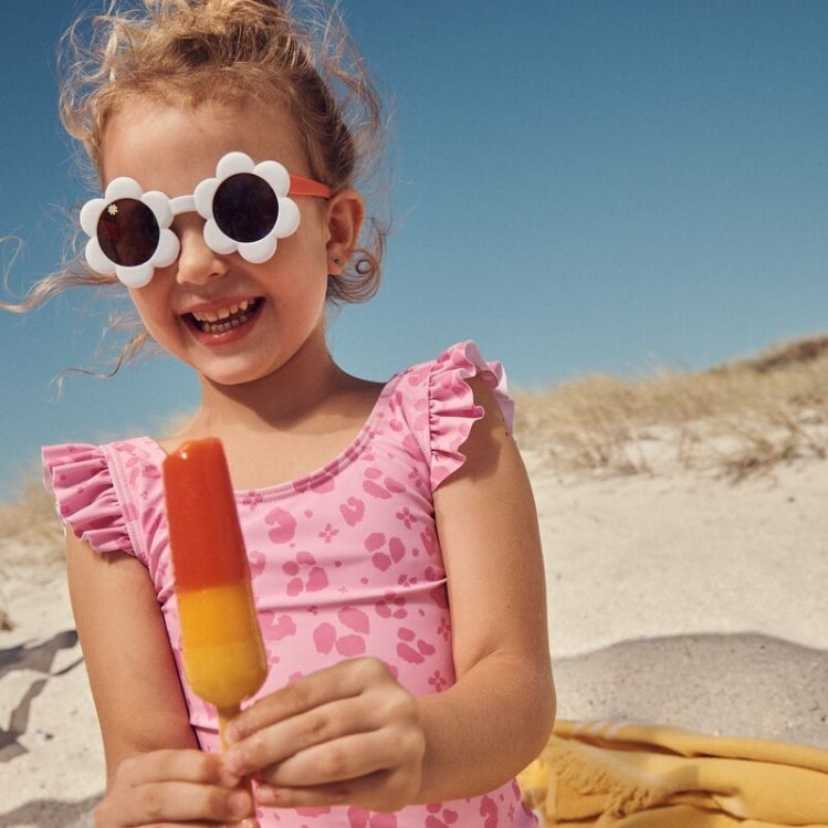 Little girl wearing swimming costume with sunglasses and beach towel eating an ice lolly
