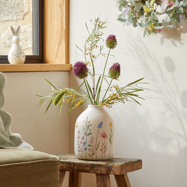 Bed with Easter bedding with bunnies, carrots and flowers on it. On the bedside table, there is a vase with flowers in it.