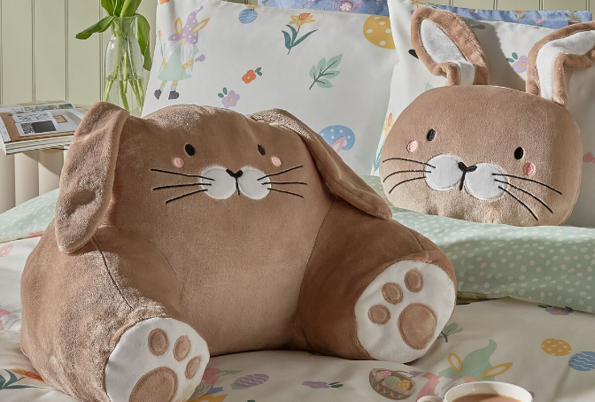 Bunny cuddle cushion and bunny cushion on top of a bed with Easter themed bedding.