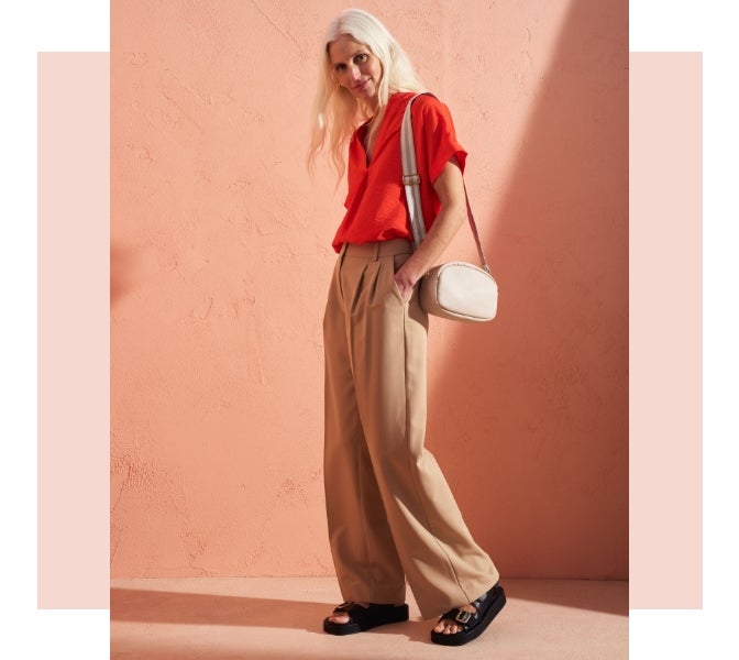 Woman wearing beige wide leg pleated trouser with a burnt orange short sleeved blouse and platform sandals with buckles